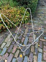 Full view of tubular metal butterfly chair frame standing on cobblestone path