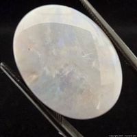 Front view of oval cabochon opal held by tweezers