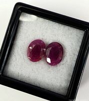 Two oval faceted rubies in display box, top view