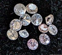 Group of round brilliant fancy-color diamonds on black background, illustrating size and cut