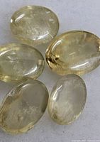 Five views of an oval cabochon pale yellow gemstone on white background