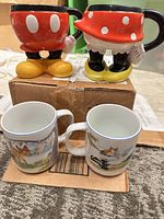 Two figural Mickey and Minnie mugs on top of two small animal character mugs