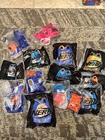 All twelve Nerf Happy Meal toys on carpet, showing sealed bags and one loose pink toy