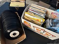 Box of unsleeved 45s, carry case, and sleeved records visible