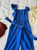 Blue jumpsuit with fabric belt displayed on bed