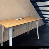 Full view of woodgrain Branch desk with white legs against wall