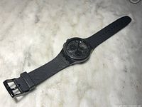 Black Swatch chronograph watch full view on marble surface