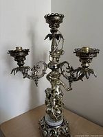 Full view of one silver-plated three-arm cherub lamp