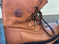 Left side view of brown Toboggan boots showing suede shaft, lace hooks, maple leaf logo