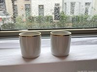 Two white porcelain espresso cups with gold rims on windowsill