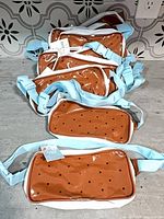 Stack of twelve identical ice-cream-sandwich fanny packs with blue straps