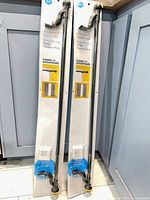Two packaged Room Essentials twist tension rods leaning against cabinet