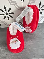 Front view of both slipper pairs showing Santa design and tags