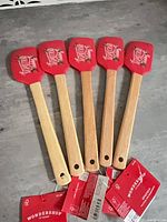 Five identical red silicone spatulas with tags displayed on countertop