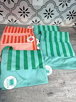Six striped kids aprons laid out, showing both colorways and front pockets