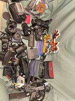 Overview of entire lot spread on surface showing multiple cameras, lenses, accessories and PS4 game