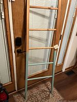 Full view of wooden decorative ladder leaning against door showing natural wood and painted lower section