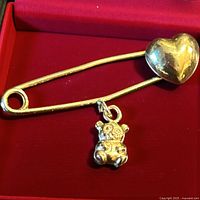 Front view of gold safety pin showing heart and teddy bear charm