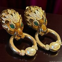 Front view of both lion head door knocker earrings showing rhinestones, green eyes and faux pearl cabochons