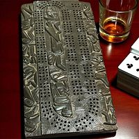 Top view of metal cribbage board on table, showing relief design and scoring holes