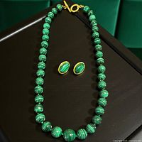 Necklace laid out in oval with earrings above clasp on dark surface