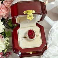 Ring in open red wooden display box, showing oval red center stone and CZ halo