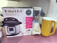 Instant Pot IP-DUO60 V3 box beside Hamilton Beach G32150 blender