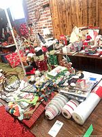 Wide view of assorted Christmas decorations on table including lights, ribbons, figurines, ornaments, linens, gift boxes