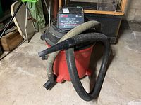 Red Craftsman shop vacuum with two hoses coiled on top