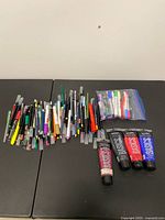 Lot overview showing four Liquitex paint tubes, large grouping of assorted pens, markers and pencils, and a zip bag with additional pens