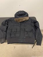 Full view of front of black Bench jacket showing pockets, ribbed hem and hood with faux fur