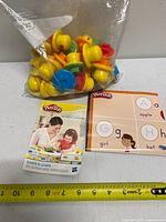 Bag containing multiple yellow stampers, booklet and learning mat laid out with measuring tape for scale