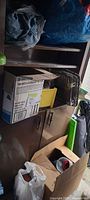Overall lot in cabinet: cardboard boxes, yellow bin, spray can, blue IKEA bag, grey cloth bundle