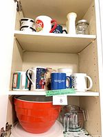 Cabinet shelf with ceramic striped measuring cups and additional kitchen mugs visible