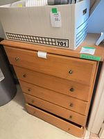 Front view showing 5-drawer light wood dresser, lower drawer misaligned
