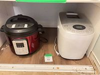 Red pressure cooker and white bread maker on shelf
