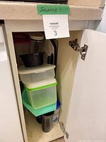 Cabinet interior showing stacked green-lid containers, black bowl, travel mugs