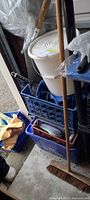 White bucket on blue crate, extension cord, broom handles visible