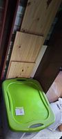 Clear plastic bin with green lid beside pine boards