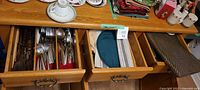 Three drawers showing flatware, linens and placemats