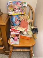 Overview of all items on chair – doll, boxed Little Live Pets pig, boxed Pop the Pig game, plush toy, flat orange-edged item