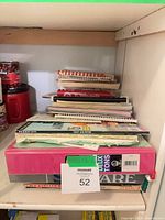 Stack of spiral-bound cookbooks and booklet manuals on shelf