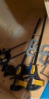 All clamps laid out inside wooden cabinet: two long bar clamps, two short bar clamps, four C-clamps
