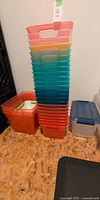 Stack of multi-colored translucent plastic totes with handles beside additional square and lidded bins