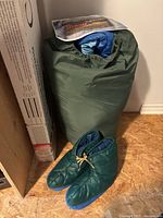 Rolled sleeping bag in green sack beside green insulated booties