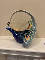 Left side of Franz Peacock Splendor teapot showing sculptural handle and tail feather details