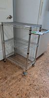 Full view of chrome wire cart showing three shelves, handle, casters