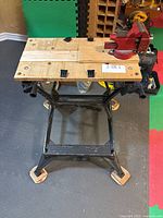 Full view of Black+Decker Workmate 200 folding workbench with red bench vise mounted and wood risers under legs