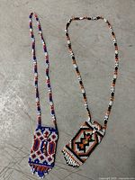 Two necklace pouches laid out showing full straps and geometric beadwork