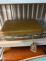 Closed caramel Samsonite suitcase on shelf showing exterior and attached keys